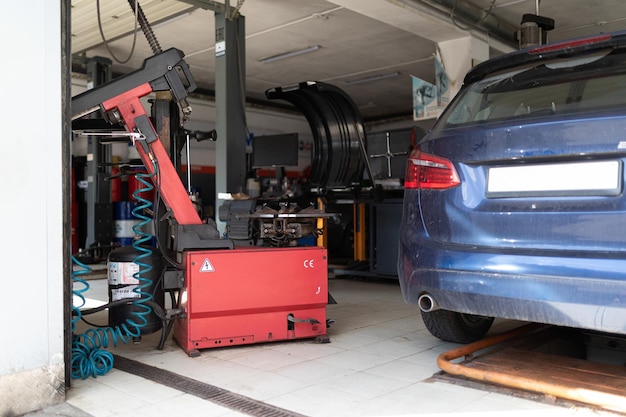 Photo of a machine for wheels and repairing tires of a car on the background of the back of a blue passenger car at a service station being repaired