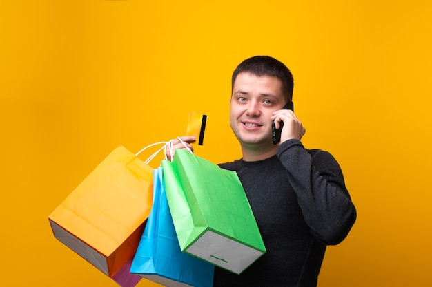 Photo of man shopper with paper bags bank card and phone in hand