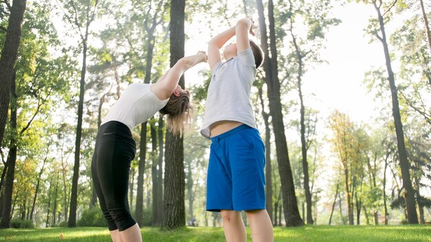 Photo of middle aged mother with her teenage boy child doing yoga and breathing exercises at park. Family taking care of thir mental and physical health while doing sports