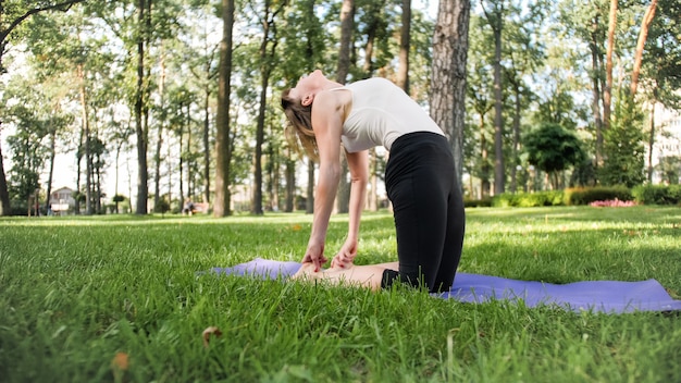 Photo of middle aged woman practicing yoga or fitness on fresh green grass at park. Female physical and mental health. Person in meditation and harmony pf body and soul