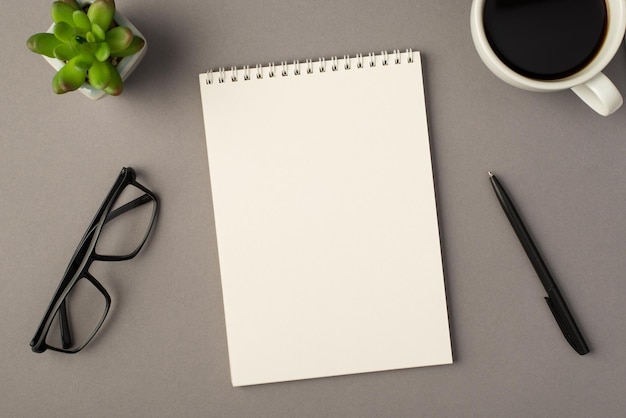 Above photo of notebook green plant glasses cup of coffee and black pen isolated on the grey background