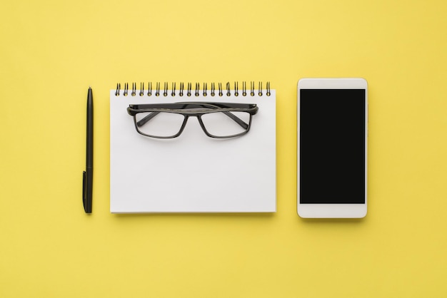 Photo overhead of notebook phone and black pen isolated on the yellow background