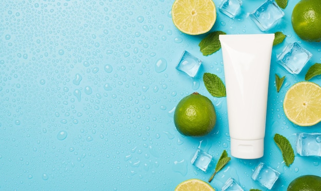 Above photo of pile of limes cubes of ice drops mint and tube of cream isolated on the blue background with blank space