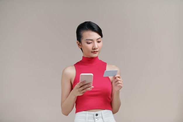 Photo of pleased young woman posing isolated using mobile phone holding debit card