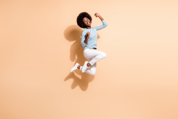 Photo portrait of astonished african american girl jumping up cheering screaming isolated on pastel beige colored background