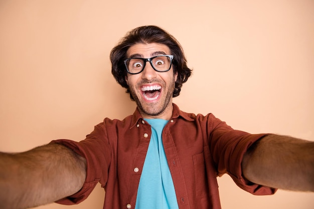 Photo portrait of excited guy taking selfie isolated on pastel beige colored background