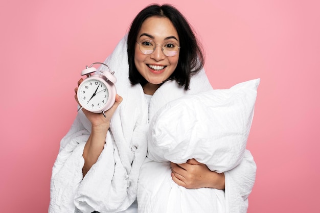 Photo portrait of happy asian girl hugging pillow and holding alarm clock