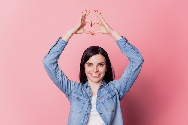 Photo portrait of romantic girl showing heart with fingers symbol of love valentine day isolated on pastel pink color background