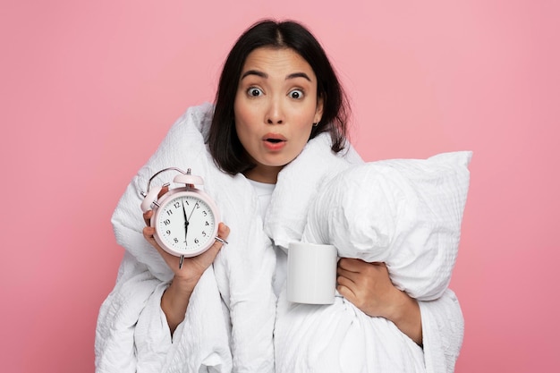 Photo portrait of surprised girl holding pillow and alarm clock with shocked face