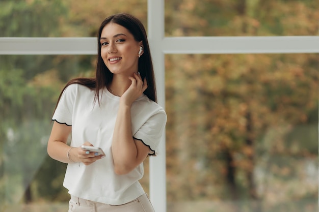 Photo portrait woman in white shirt wearing wireless earbuds enjoying music relaxing at home