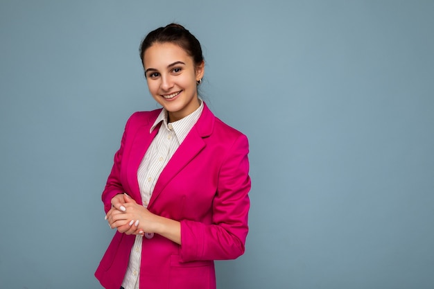 Photo portrait of young pretty beautiful happy smiling brunette woman with sincere emotions wearing casual white shirt and stylish pink jacket isolated over blue background with copy space