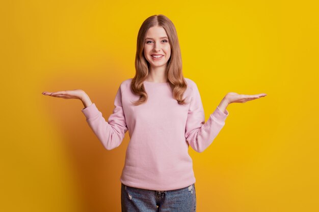 Photo of positive cheerful girl palms hold empty space compare concept on yellow background