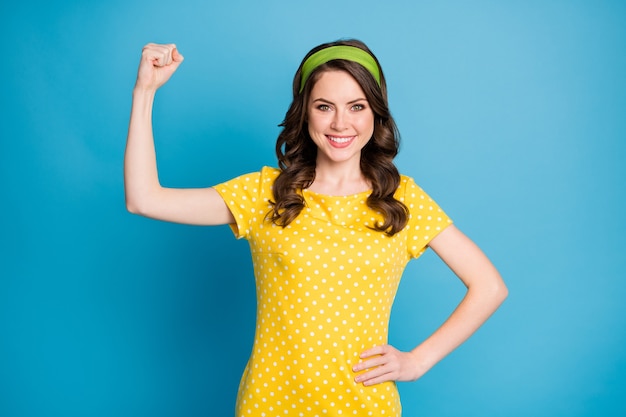 Photo of positive cheerful girl show her hand muscles wear polka-dot outfit isolated over blue color background