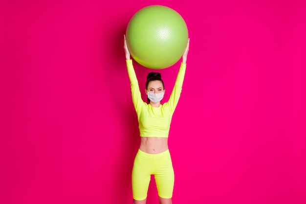 Photo of positive young sportswoman raise fit ball up wear medical mask  isolated pink shine color background