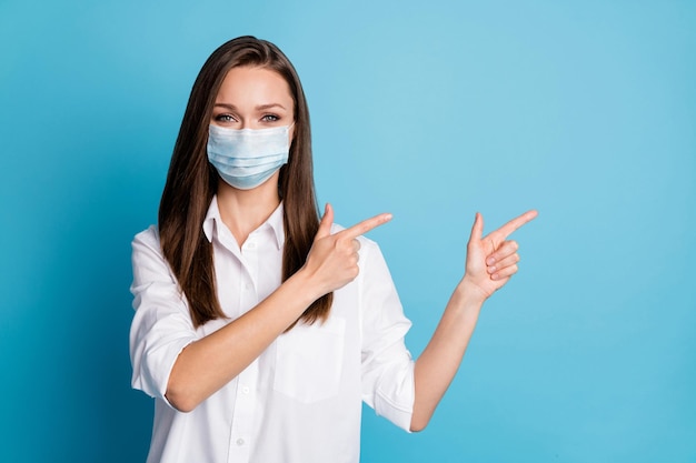 Photo of pretty lady good mood direct fingers side empty space wear mask white shirt isolated blue color background