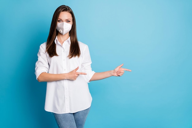 Photo of pretty sales manager lady direct fingers side empty space wear mask white shirt jeans isolated blue color background