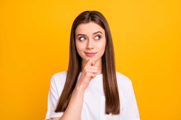 Photo of pretty wondered lady long hairdo look side empty space see interesting advert banner finger on chin wear casual white t-shirt isolated vivid yellow color wall