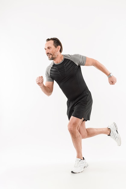 Photo in profile of content energetic sportsman 30s wearing shorts and t-shirt smiling and running marathon or doing workout