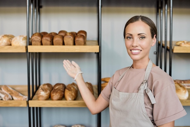 Photo realistic digital collage of young baker in apron pointing at shelf