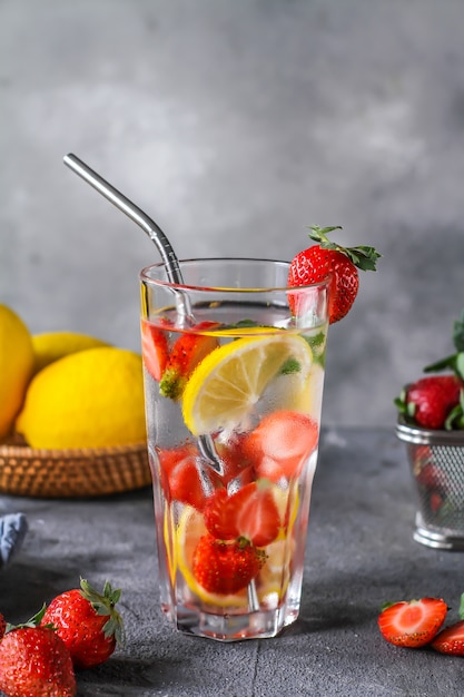 Photo of refreshing summer iced cold drink. Strawberry infused waters. Mineral water with fresh strawberries lemon with a grey background. Detox water with strawberry lemon. Copy space.