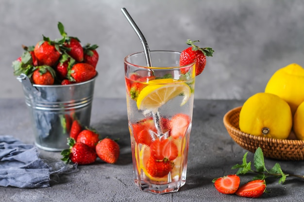 Photo of refreshing summer iced cold drink. Strawberry infused waters. Mineral water with fresh strawberries lemon with a grey background. Detox water with strawberry lemon. Copy space.