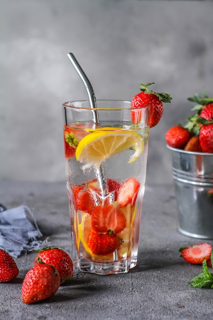 Photo of refreshing summer iced cold drink. Strawberry infused waters. Mineral water with fresh strawberries lemon with a grey background. Detox water with strawberry lemon. Copy space.