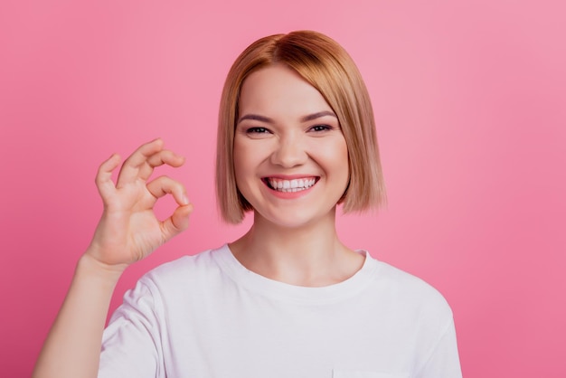 Photo of reliable positive charming blonde lady show okey sign wear white t-shirt isolated on pink background