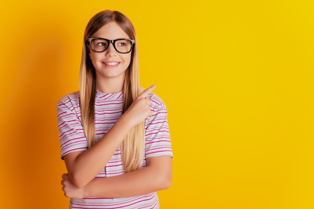 Photo of schoolgirl pointing blank space isolated on yellow background