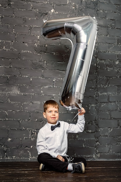 photo session with a ballon 7 years old. Silver ballon with number 7. A boy at a photoset in the studio