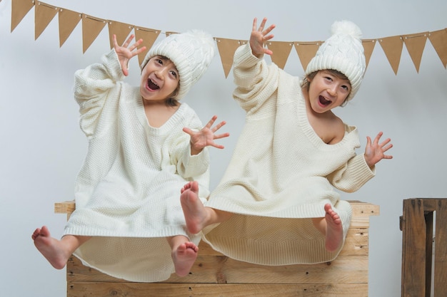 Photo session with twins dressed in white sweaters and wool caps posing and playing with confetti