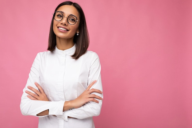 Photo shot of beautiful positive smiling young brunette woman wearing casual clothes and stylish optical glasses isolated over colorful background looking at camera. empty space