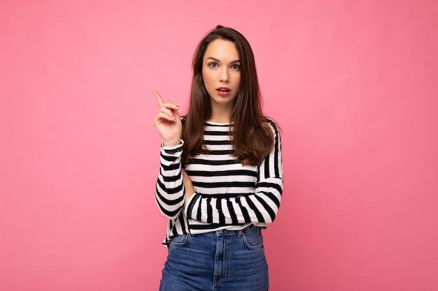 Photo shot of cute attractive pretty thoughful dreaming young brunette woman wearing casual striped longsleeve isolated over colorful background with copy space.