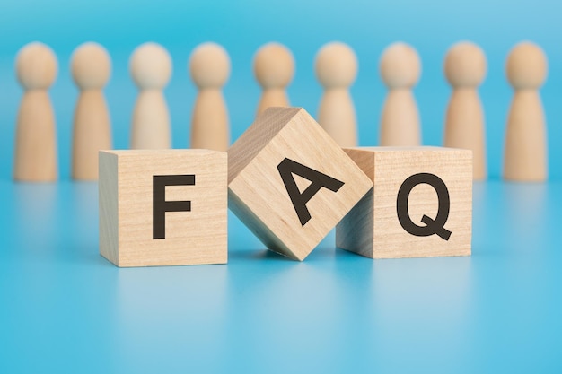 the photo showcases three small wooden cubes on a blue backdrop inscribed with letters F A Q wooden figurines blurred in the background resemble a team