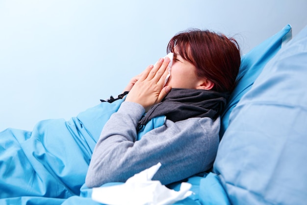 Photo of sick brunette blowing her nose in paper handkerchief lying in bed