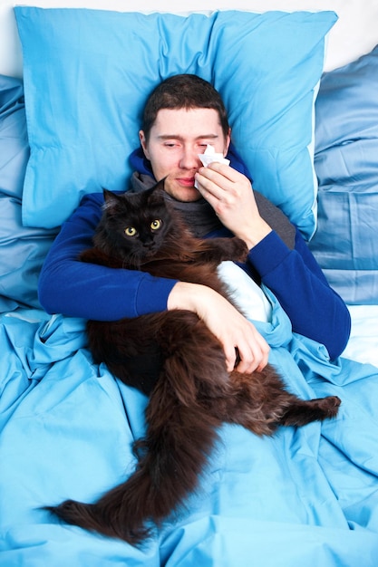 Photo of sick man in scarf with cat lying in bed