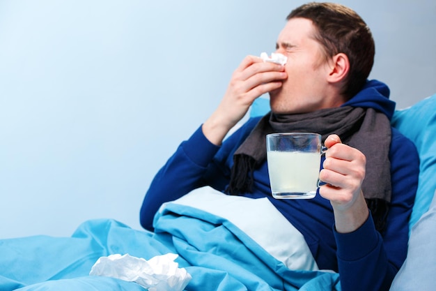 Photo of sick man in scarf with cup of medicine lying in bed