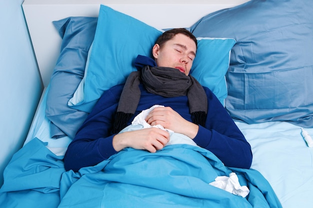 Photo of sick man in scarf and with handkerchiefs lying in bed