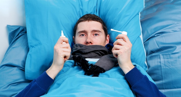 Photo of sick man with sprays in hands lying in bed