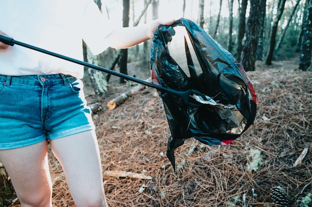 Photo of side of girl picking up garbage in bag on the forest during a sunsetEnvironmental garbage pollutionNature cleaning volunteer ecology green concept