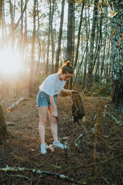 Photo of side of girl picking up garbage in bag on the forest during a sunsetEnvironmental garbage pollutionNature cleaning volunteer ecology green concept