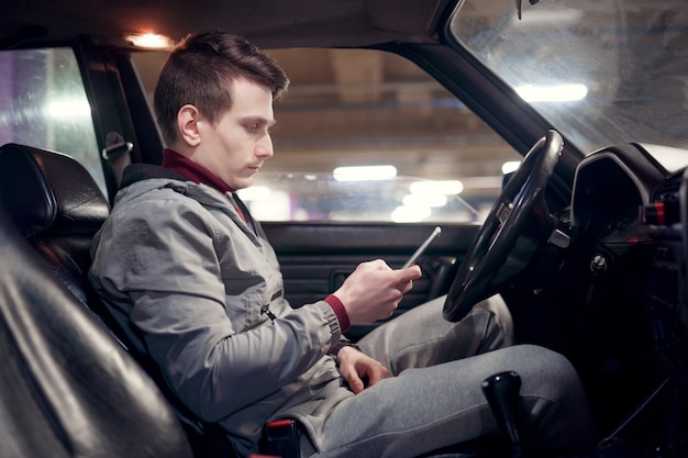 Photo of side of male driver with phone in hands sitting in car