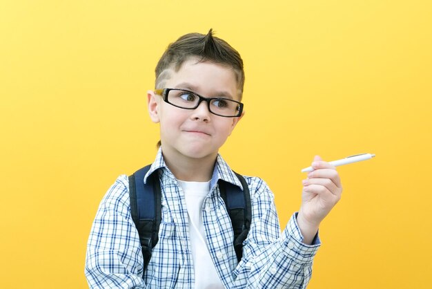 Photo of a smart schoolboy holding a pen in a white shirt on a yellow background. place for your text, copy space