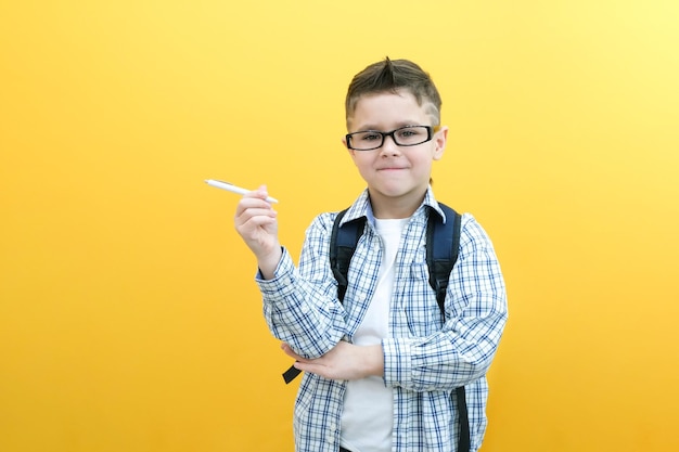 Photo of a smart schoolboy holding a pen in a white shirt on a yellow background place for your text copy space