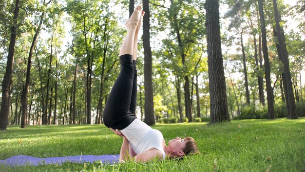 Photo of smiling happy woman 40 years old doing yoga exercises on fitness mat at forest. Harmony of human in nature. Middle aged people taking car of mental and physical health