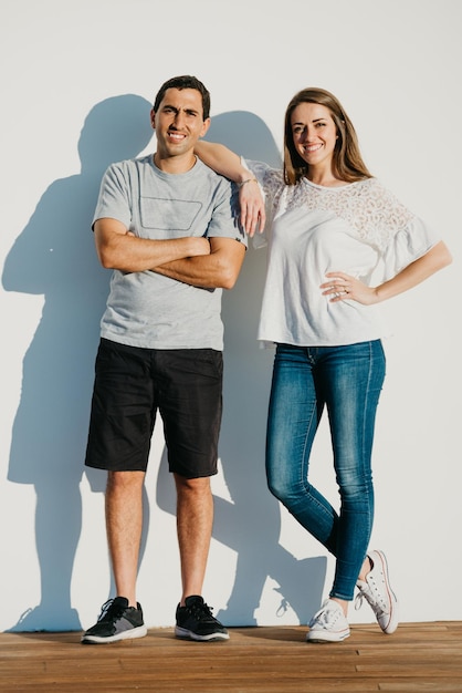 A photo of a smiling woman is leaning her elbow on the shoulder of a Hispanic man near the pier