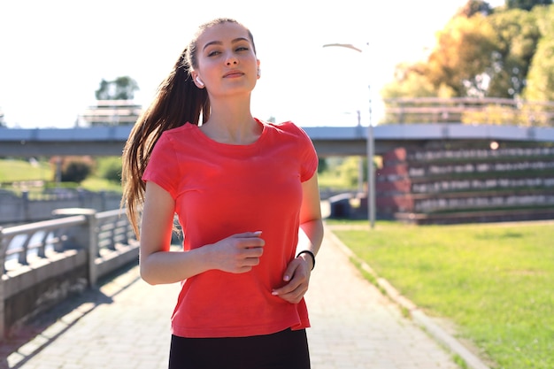 Photo of sporty slim woman wearing sportswear listening music with earphones while running working out near city riverfront.