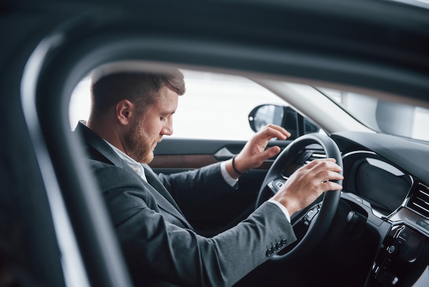 Photo through the glass. Modern businessman trying his new car in the automobile salon.