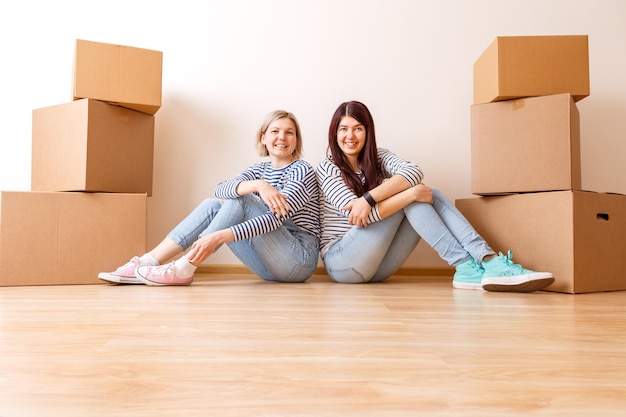 Photo of two girls sitting on floor among cardboard boxes