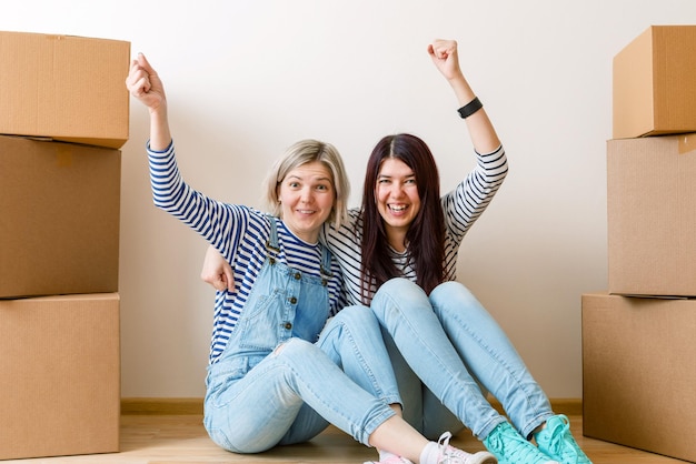 Photo of two girls sitting on floor among cardboard boxes