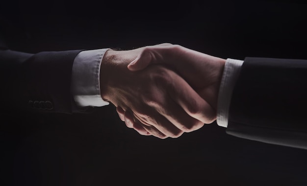 Photo of two men in suits shaking hands on a black background